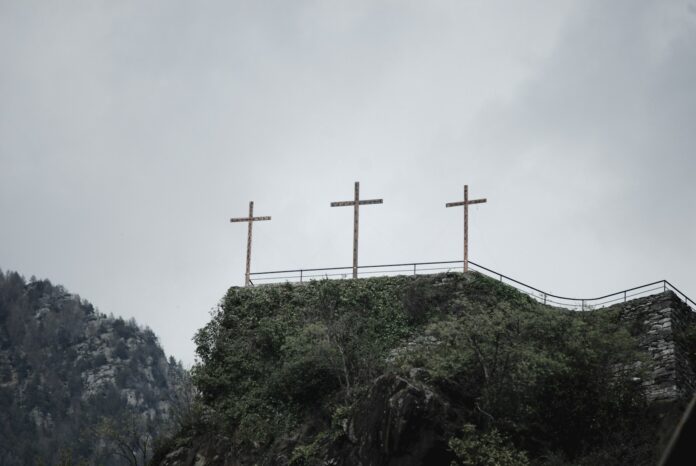 three crosses on top of a hill on a cloudy day
