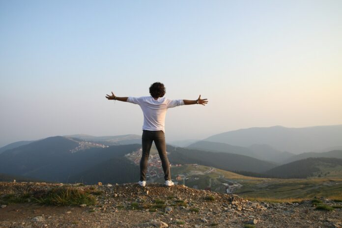 Photo by Catalin Pop man in white t-shirt and grey pants standing on top of hill