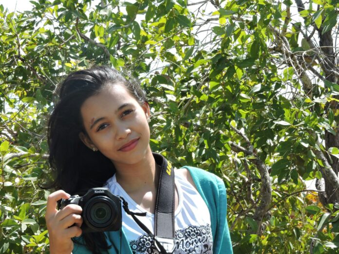 Photo by Gleive Marcio Rodrigues de Souza a woman holding a camera in front of a tree