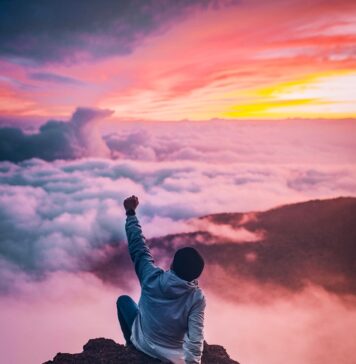 Reflita sobre o poder man sitting on mountain cliff facing white clouds rising one hand at golden hour