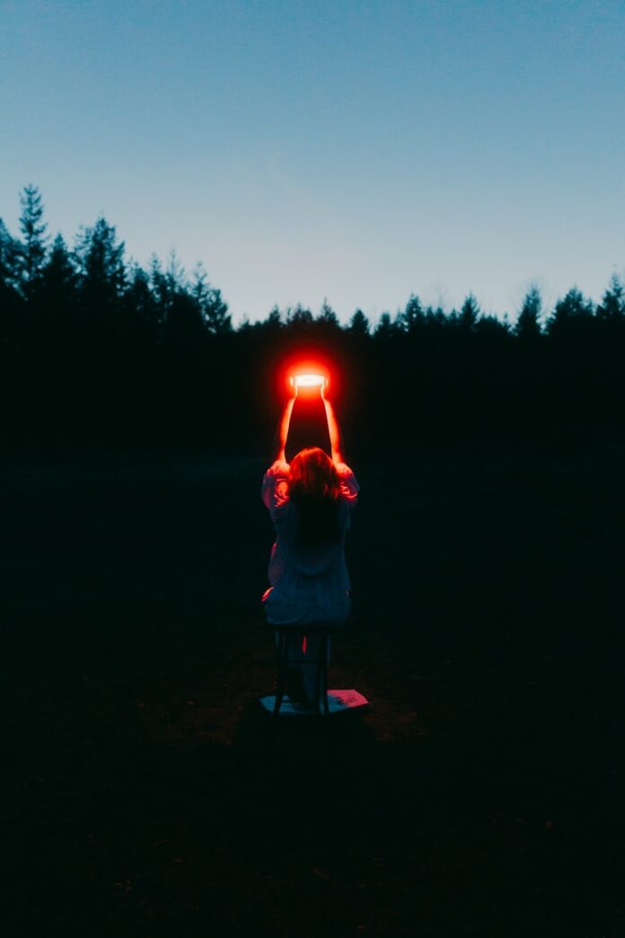 A person holding a glowing red light outdoors at dusk.