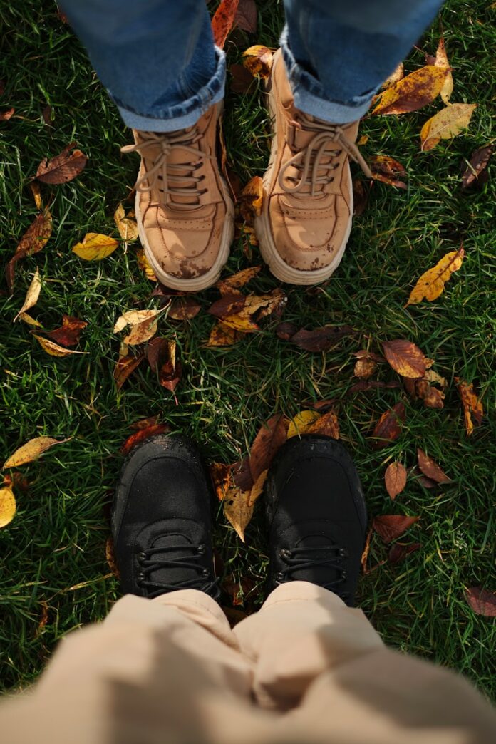 Photo by Dmitry Spravko Two pairs of feet standing on grass with fallen leaves.