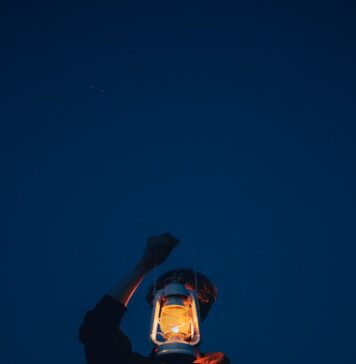 Um passo suficiente Person holding a lit lantern against a dark blue sky