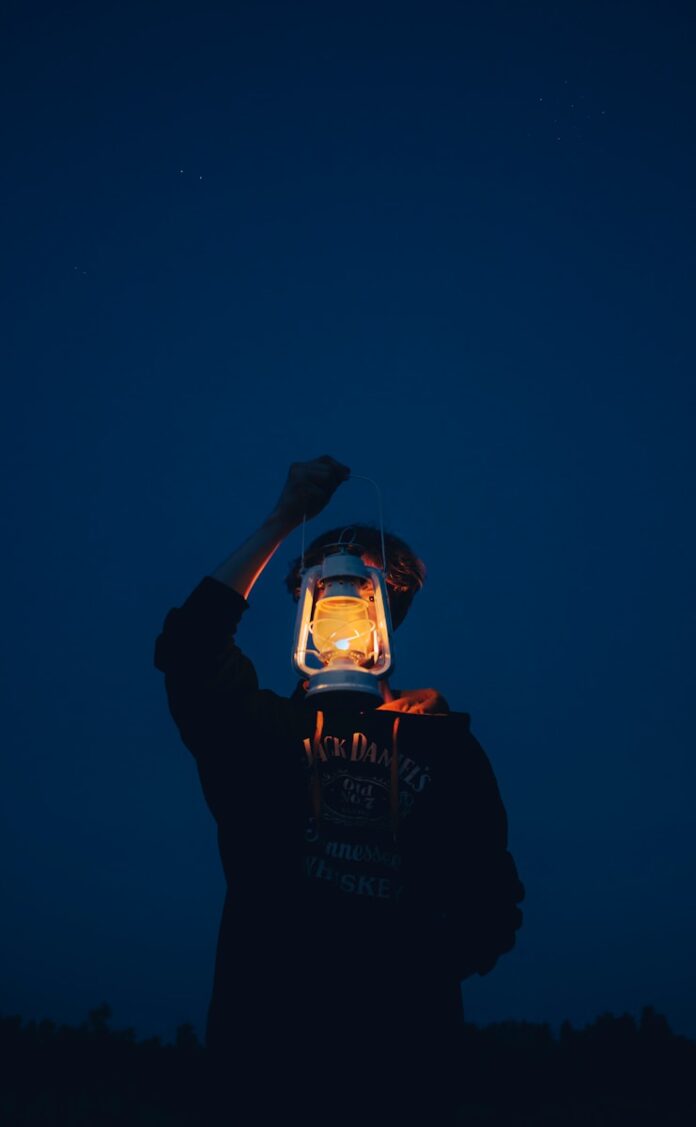 Person holding a lit lantern against a dark blue sky