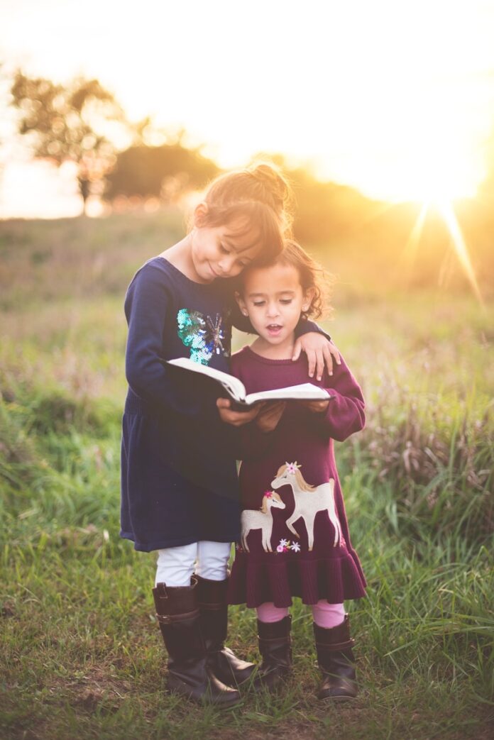 Photo by Ben White girl's left hand wrap around toddler while reading book during golden hour