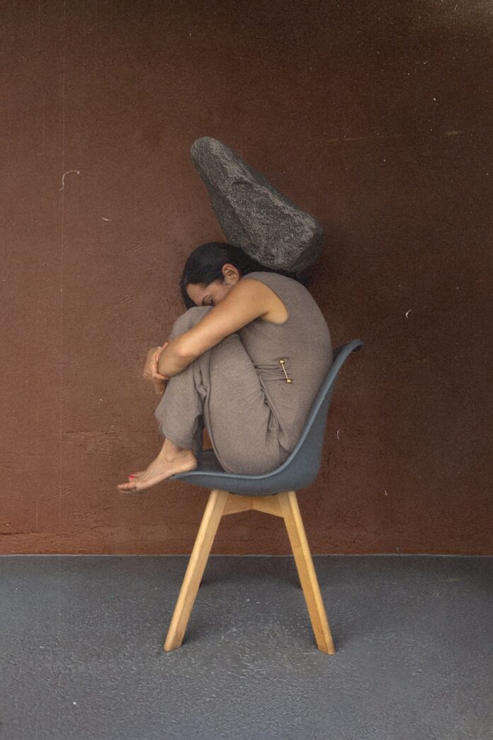 Woman curled on chair with rock overhead