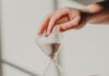 Tempo na ampulheta two hands holding a sand glass in front of a window