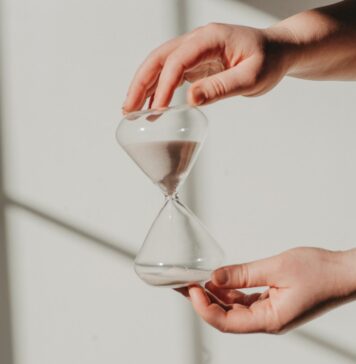 Tempo na ampulheta two hands holding a sand glass in front of a window