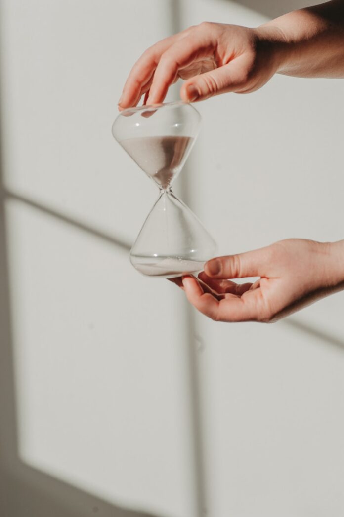 two hands holding a sand glass in front of a window