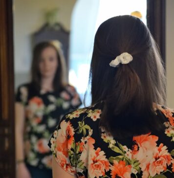 Você precisa ser você woman wearing black and multicolored blouse and blue denim jeans facing mirror inside white concrete room