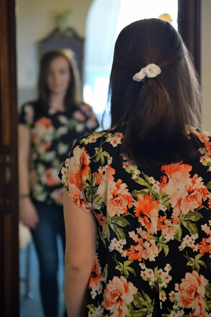 Photo by Taylor Smith woman wearing black and multicolored blouse and blue denim jeans facing mirror inside white concrete room