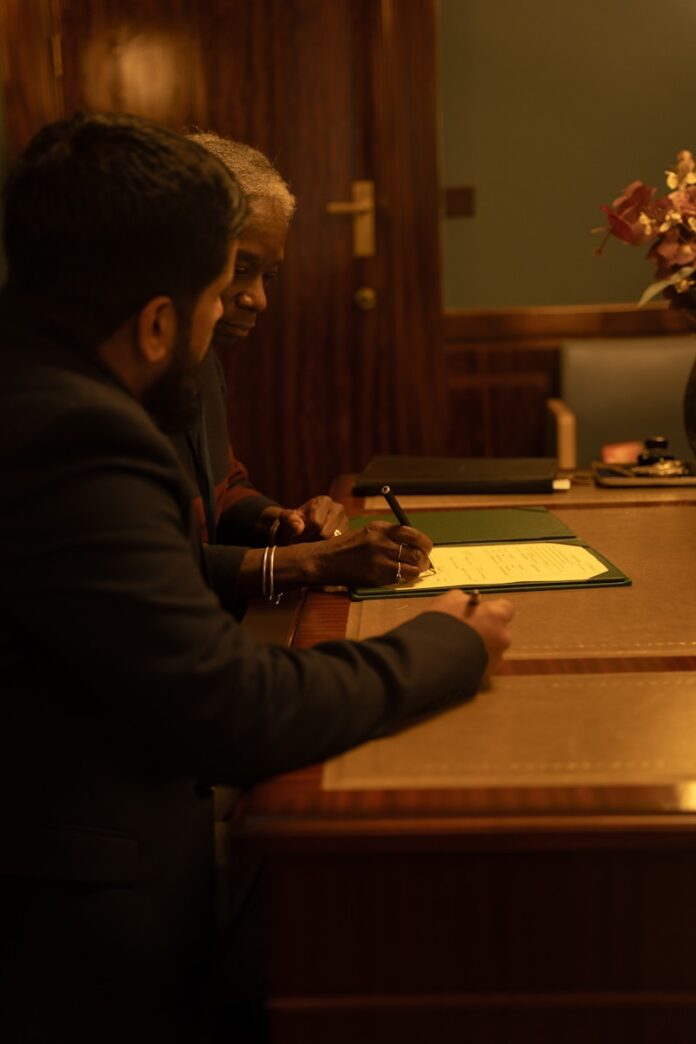 Two people are signing a document at a desk