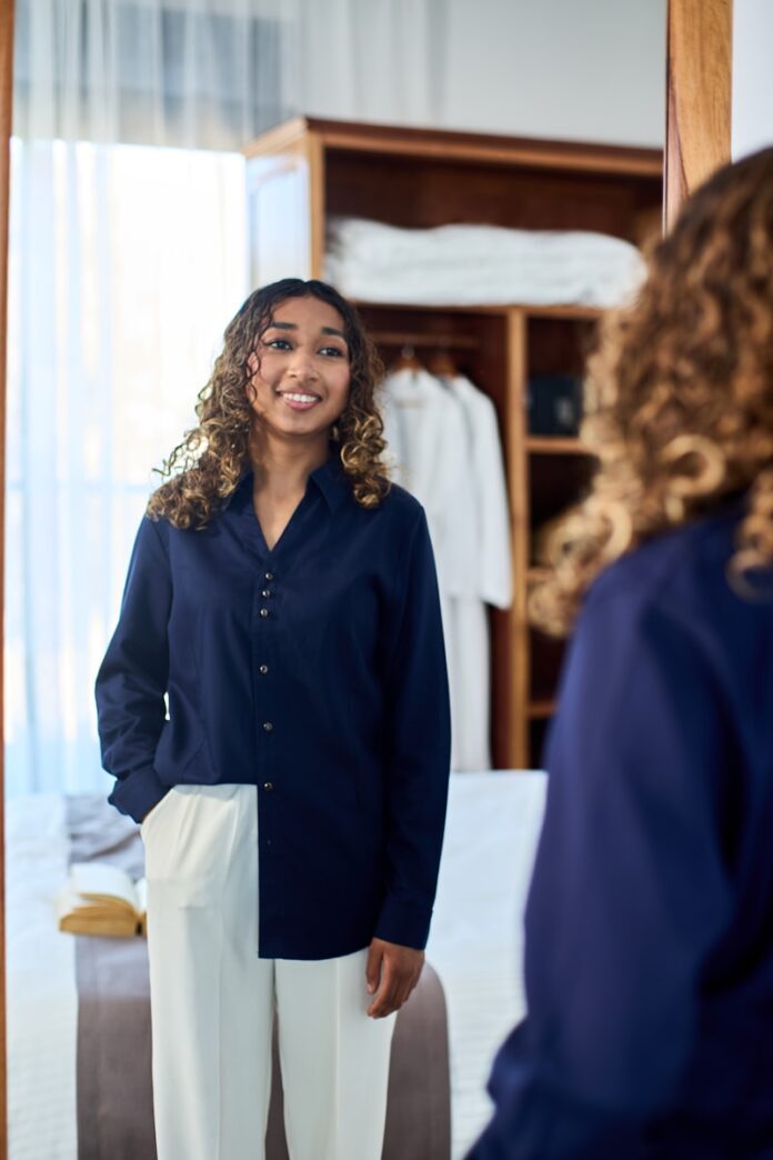 Photo by Shane Ryan Herilalaina Woman in navy shirt and white pants smiles at mirror