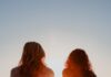 Uma presença garantida two woman sitting on beach sand while facing sunlight