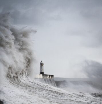 Confie no Capitão a lighthouse surrounded by a huge wave in the ocean