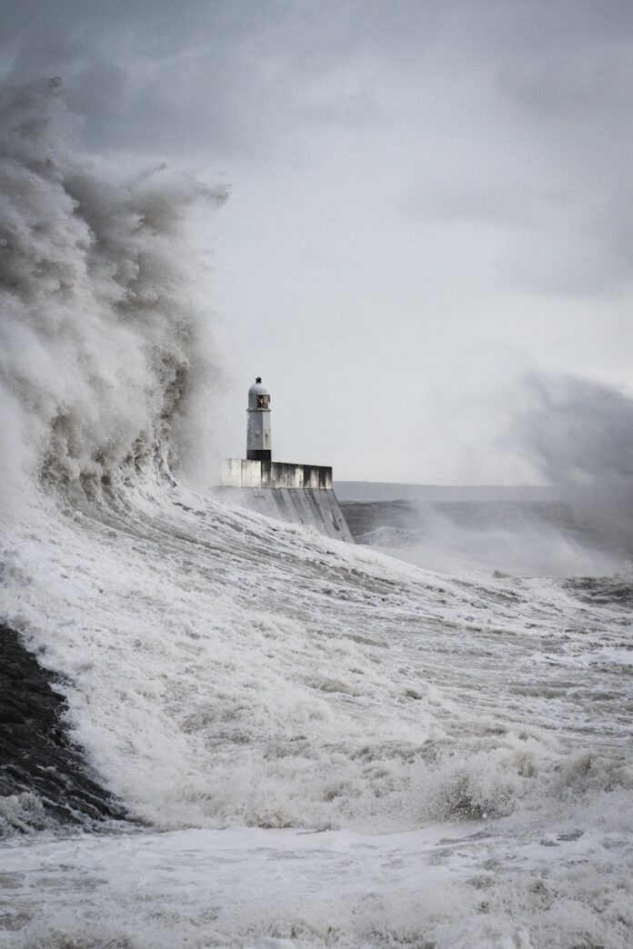 Photo by Marcus Woodbridge a lighthouse surrounded by a huge wave in the ocean