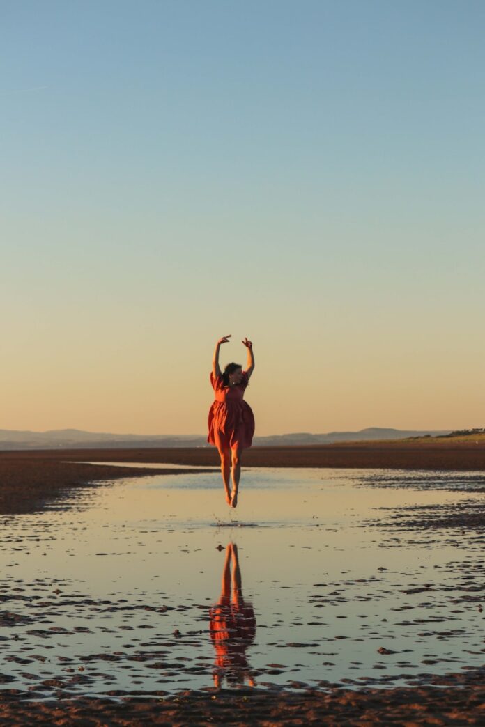 Photo by Phoebe Dill a woman in a red dress is running on the beach