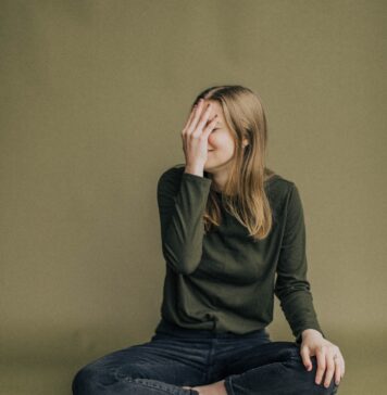 Emoções de orgulho e vergonha woman in black long sleeve shirt and blue denim jeans sitting on brown wooden chair