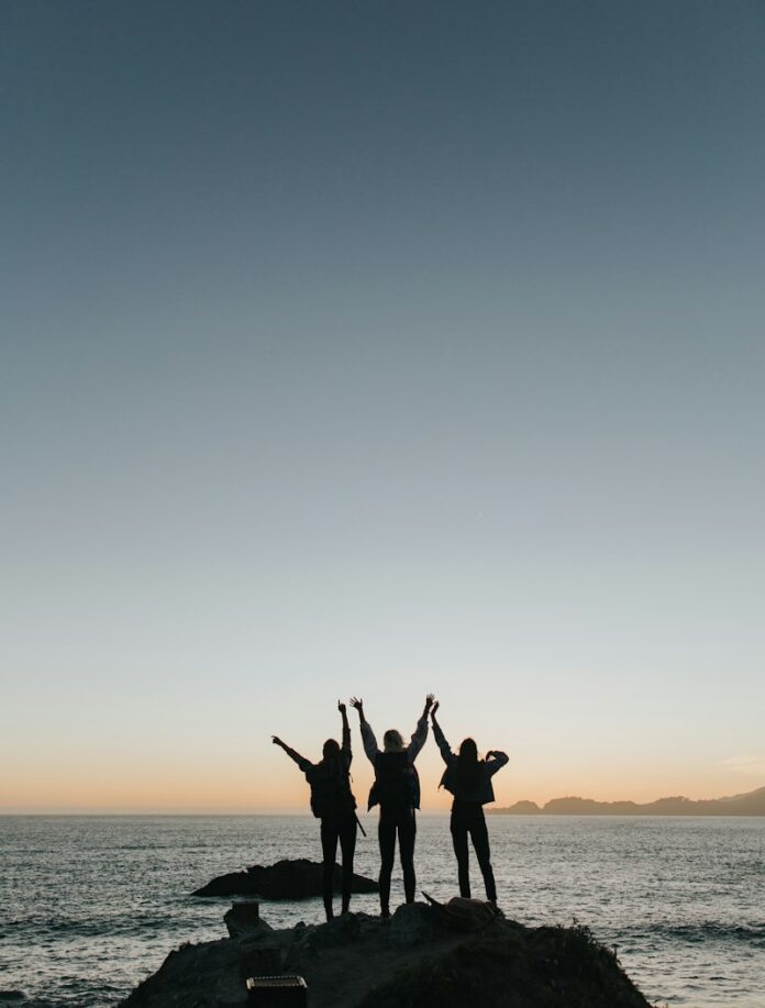 Photo by Ivana Cajina silhouette photography of persons raising hands while standing on island