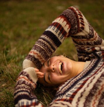 Uma vida de alegria e abundância woman in brown and white sweater lying on green grass field during daytime