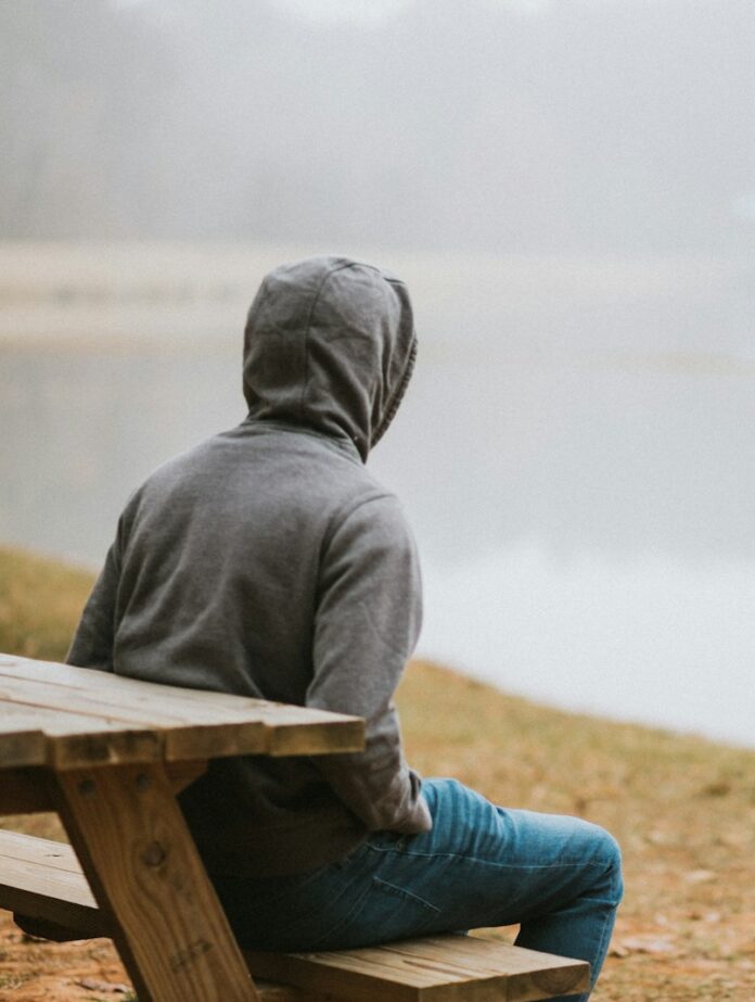 person in gray hoodie sitting on picnic table staring at the fog during daytime
