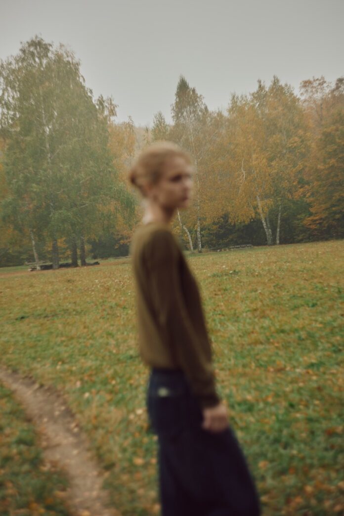 A person in a brown sweater standing in a misty autumn forest clearing